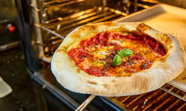 Leckere Pizza Margherita mit frischem Basilikum wird im Backofen gebacken. Der Teig ist goldbraun, die Tomatensauce blubbert.