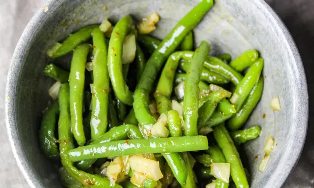 En skål med glansiga, gröna haricots verts blandade med bitar av vitlök och kryddor.