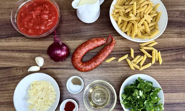 Składniki na pyszny makaron z chorizo: pomidory, cebula, czosnek, makaron penne, śmietanka, parmezan, oliwa, przyprawy i świeża natka pietruszki.