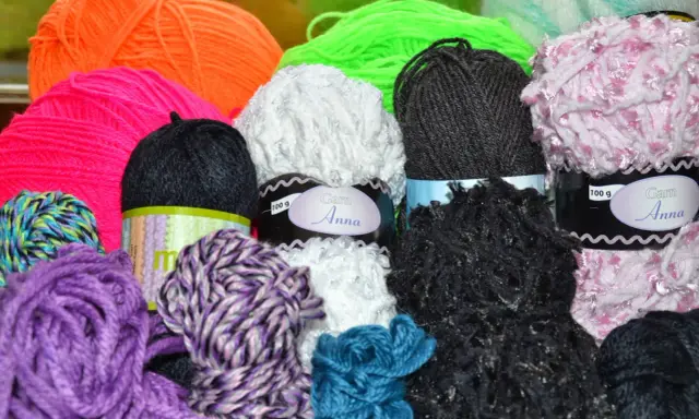 A colorful assortment of yarn balls in various textures and colors, including purple, pink, orange, green, white, black, and blue.