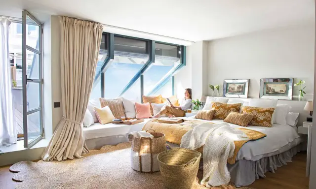 Habitación acogedora con cama grande, cojines coloridos y una zona de lectura junto a la ventana. Ideas para decorar habitacion con estilo natural.