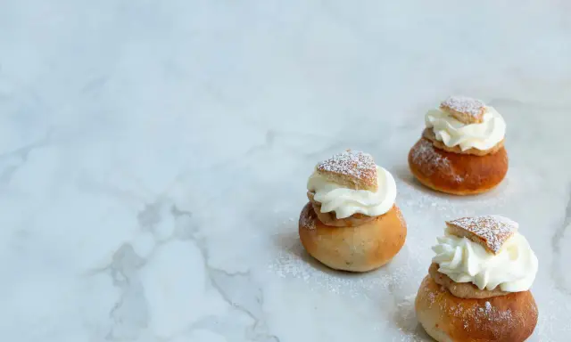 Tre semlor utan mandelmassa, toppade med vispgrädde och pudersocker, ligger på ett marmorbord.