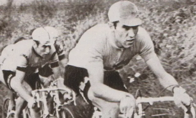Dwóch kolarzy w akcji. Na pierwszym planie widać zawodnika w czarnych spodenkach i jasnej koszulce, zdeterminowanego jak zawsze Eddy Merckx.