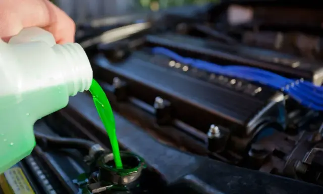 Mano vierte líquido refrigerante verde brillante en el radiador de un coche. Guía para saber como cambiar el liquido refrigerante.