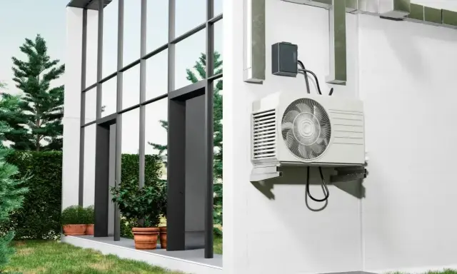Unité extérieure d'une pompe à chaleur installée sur un mur blanc, à côté d'une maison moderne avec de grandes fenêtres. Comment choisir quelle pompe à chaleur choisir pour votre maison ?