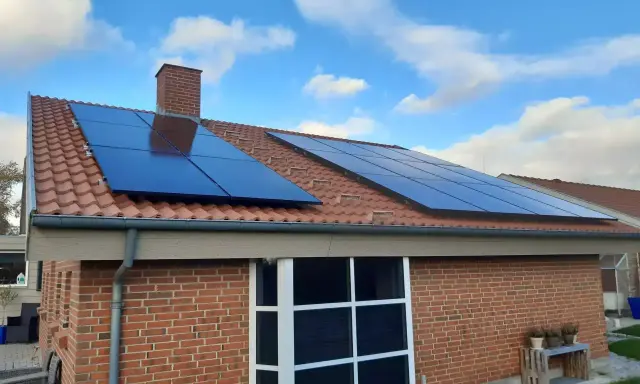 Ett tegelhus med solpaneler på taket, redo att generera egen energi. Blå himmel med vita moln.