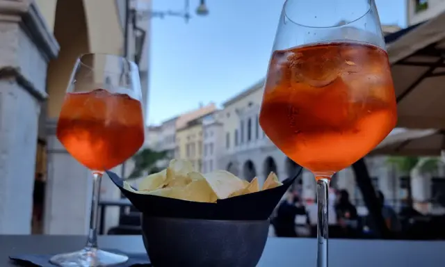 Dwa drinki Aperol Spritz i miseczka chipsów na stoliku. Czy alkohol podnosi cholesterol? To pytanie zadaje sobie wielu, delektując się takimi przekąskami.