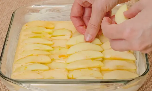 Ręce układają plasterki jabłek na cieście. Powstaje pyszne ciasto z jabłkami, gotowe do pieczenia.