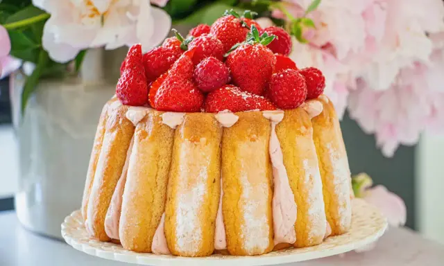 Charlotte aux fruits rouges, un délice de biscuits à la cuillère et crème rose, couronné de fraises et framboises fraîches.