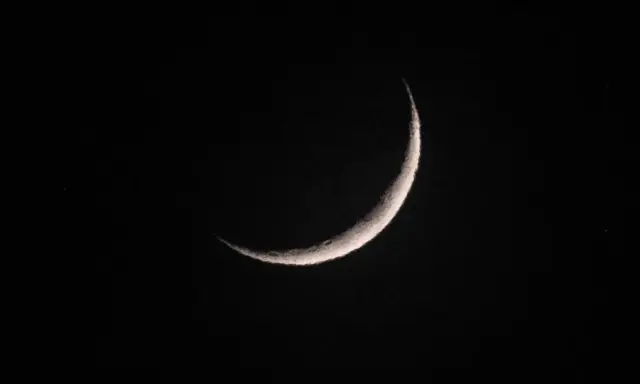 Eine schmale Mondsichel leuchtet im dunklen Nachthimmel. Sie erinnert an den Beginn von Ramadan, wann die Zeit des Fastens beginnt.