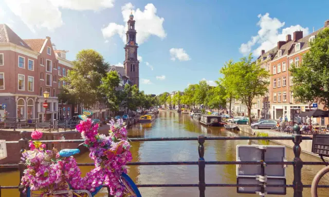 Das **beste von Amsterdam**: malerischer Kanal mit Booten, historischen Gebäuden und einem Kirchturm. Blumenverzierte Fahrräder auf einer Brücke.