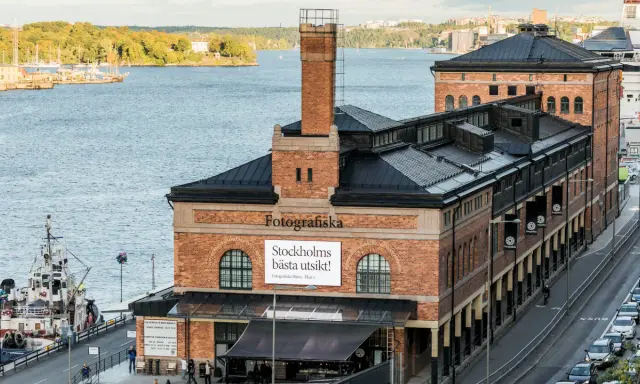 Fotografiska Stockholm vid vattnet, med en båt i förgrunden och en stadssilhuett i bakgrunden.