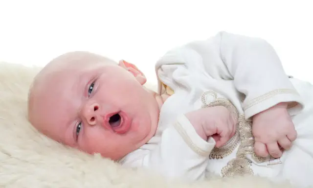 Baby mit offenem Mund, vielleicht husten. Was tun? Ein süßer kleiner Mensch auf weichem Fell.