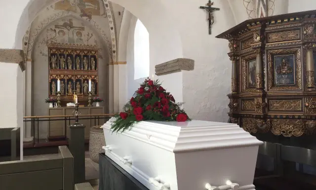 Biała trumna z czerwonymi różami w kościele. Warto wiedzieć, jak się zachować przy otwartej trumnie, by okazać szacunek zmarłemu.