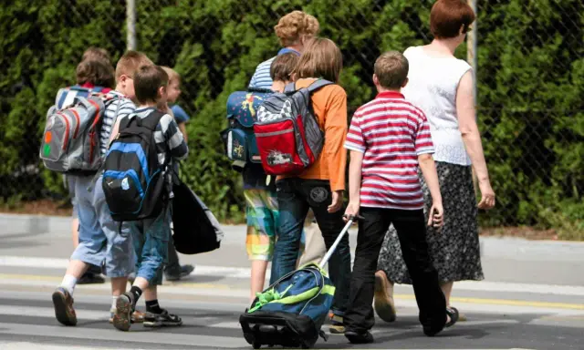 Niños con mochilas y un carrito cruzan la calle, marcando el regreso a la rutina de septiembre.