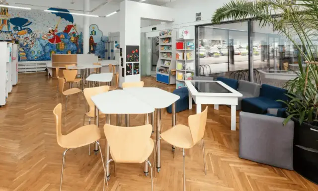 Spazi della scuola luminosi con scaffali, tavoli, sedie e un murale colorato. Un'area accogliente per imparare e giocare.