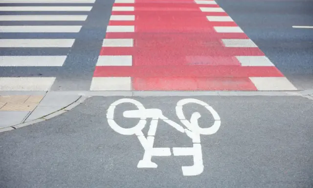 Czerwone pasy dla rowerzystów przecinają przejście dla pieszych. Symbol roweru na asfalcie zaprasza do bezpiecznej jazdy.