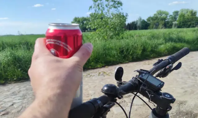Rowerzysta trzyma puszkę napoju, co sugeruje kierowanie rowerem w stanie nietrzeźwości. Na kierownicy widoczny licznik.