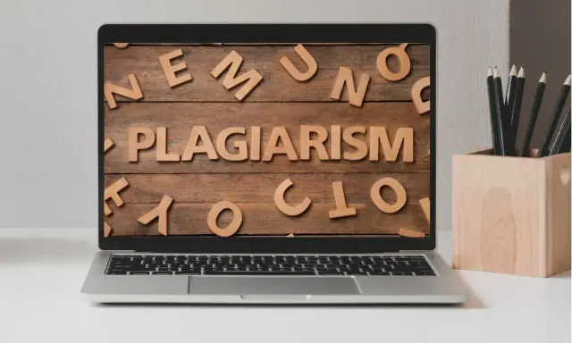Laptop z napisem "PLAGIARISM" ułożonym z drewnianych liter na tle desek.