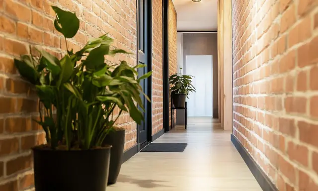 Przedpokój loft inspiracje: ceglane ściany, jasna podłoga, czarne drzwi i zielone rośliny tworzą przytulną przestrzeń.