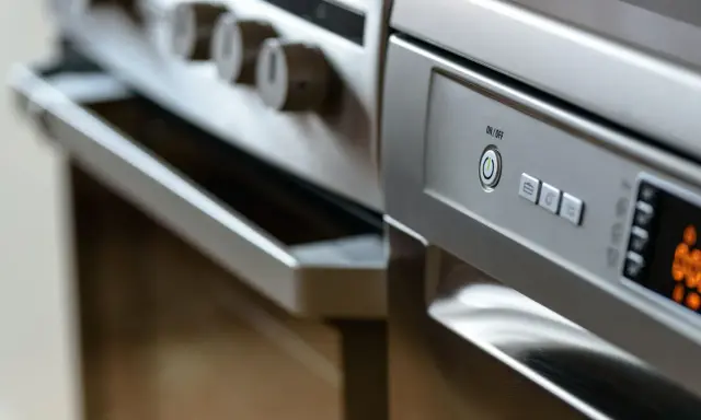 Nowoczesna kuchnia z piekarnikiem i zmywarką obok. Panel sterowania zmywarki z przyciskiem ON/OFF.