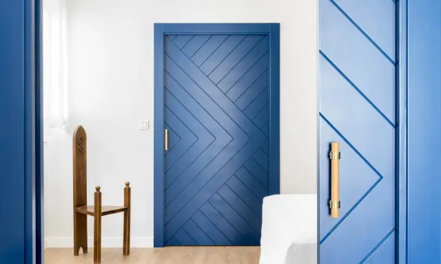 Puertas azules interiores con diseño geométrico y tiradores de madera. Una silla de madera antigua destaca junto a una de las puertas.