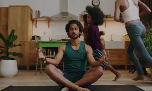 Man i lugn meditation i köket medan barn springer förbi. En lugn stund för 5 minute meditation mitt i vardagskaoset.