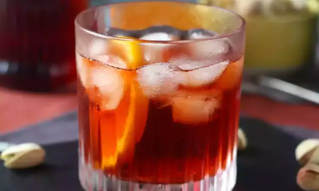 Orzeźwiający negroni sbagliato z lodem i plasterkiem pomarańczy, podany z pistacjami.