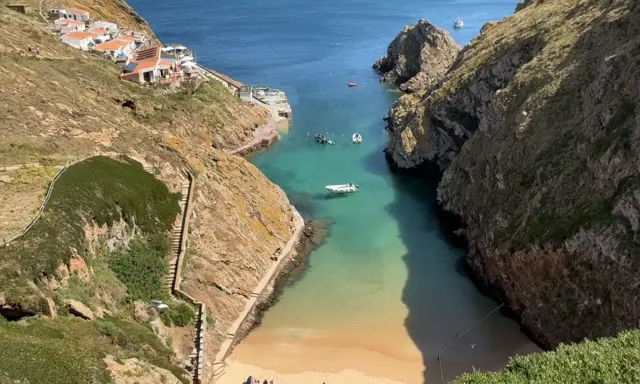 Idyllische Bucht mit weißem Sandstrand und türkisfarbenem Wasser auf den Berlengas Inseln. Kleine Boote ankern, Häuser schmiegen sich an die Felsen.