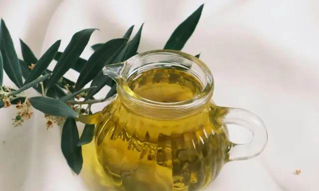 Aceite de oliva dorado en jarra de cristal, junto a rama de olivo. ¿Cuál es el aceite de oliva más suave?