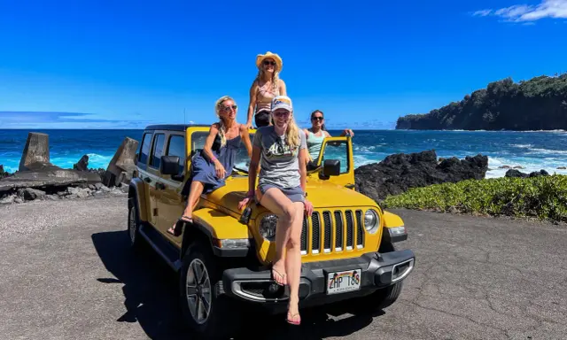Fyra glada kvinnor på en gul jeep vid havet. Drömmen om att flytta till Hawaii känns nära!