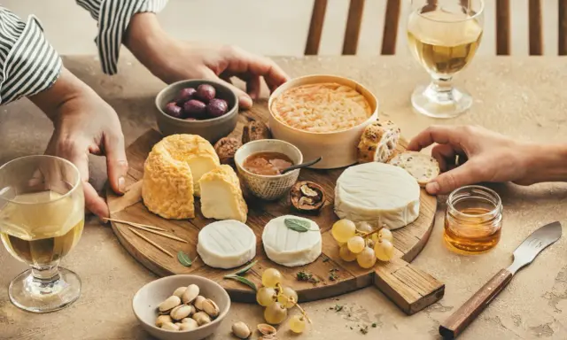 Un tableau accord vin et fromage avec divers fromages, olives, noix, raisins, pistaches et miel.