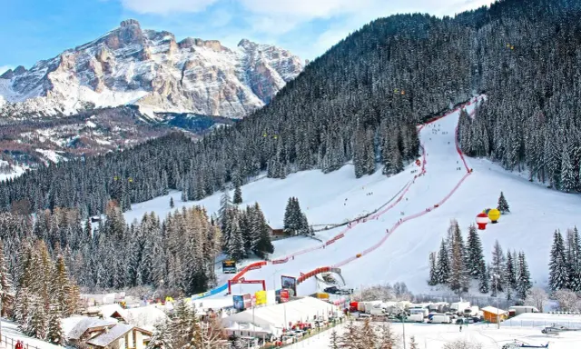Ośnieżony stok narciarski w Alta Badia z lasem i górami w tle.