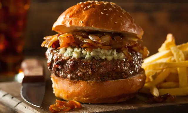 Jugosa hamburguesa con queso de cabra desmenuzado, cebolla caramelizada y papas fritas crujientes.