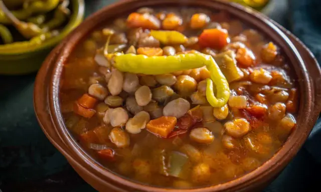 Un cuenco de barro con pochas a la navarra, un guiso reconfortante de alubias blancas, verduras y un pimiento verde.