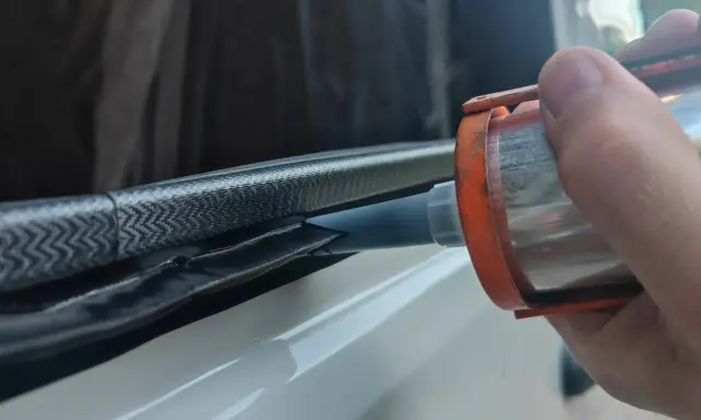 Application de mastic Sika 265 sur un joint de fenêtre de véhicule pour une étanchéité parfaite.