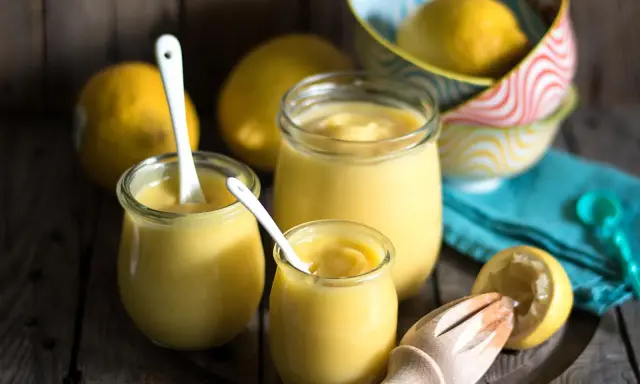 Drei Gläser mit cremigem Lemon Curd, Löffel und frische Zitronen. Perfekt für ein einfaches Lemon Curd Rezept.
