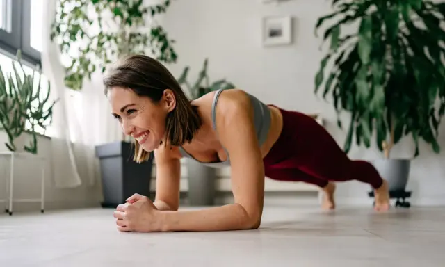 Femme souriante en plein exercice de gainage, profitant d'un moment de bien-être à la maison.