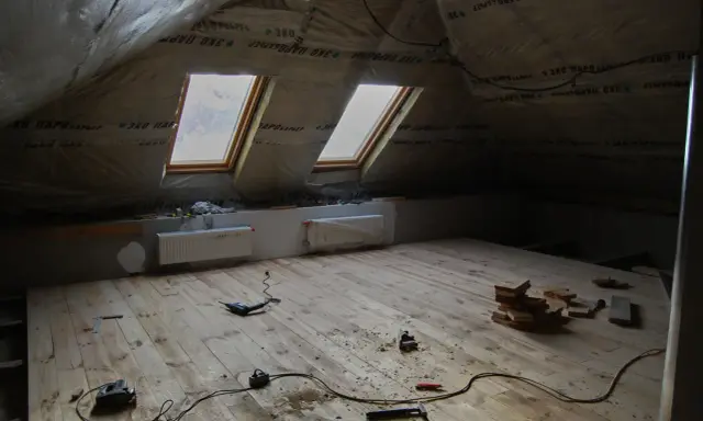 Chantier sous les combles : pose du frein vapeur, deux fenêtres de toit, radiateurs et outils sur le plancher en bois.