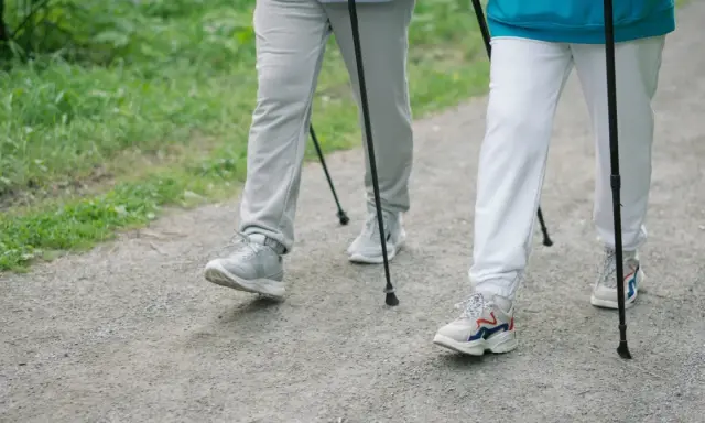 Dwie osoby maszerują z kijkami po żwirowej ścieżce, otoczone zielenią.