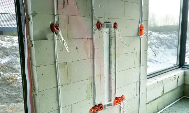 Instalacja elektryczna w ścianie z bloczków betonowych, etap prac wykończeniowych od stanu surowego zamkniętego. Widoczne puszki i przewody.