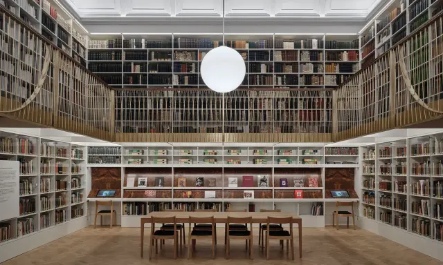 A grand library with towering bookshelves, a central reading table, and a modern globe light. This space feels like a capital photography center for learning.