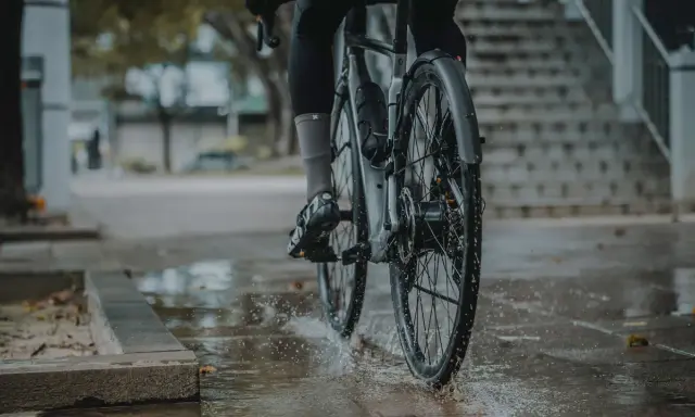 Rowerzysta w deszczu, koła rozpryskują wodę. Montaż błotnika rowerowego zapewnia suchą jazdę.