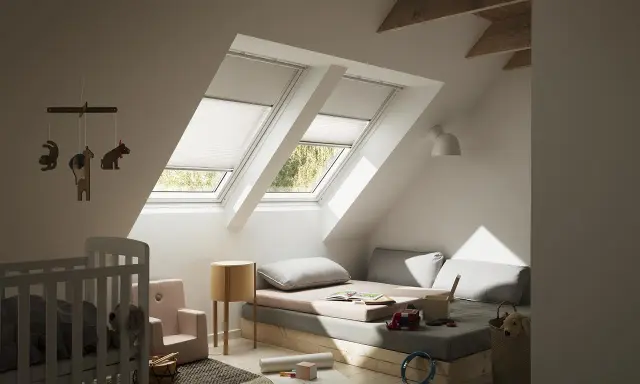 Habitación infantil con dos ventanas de tejado equipadas con cortinas para Velux caseras, cama baja, cuna y juguetes.