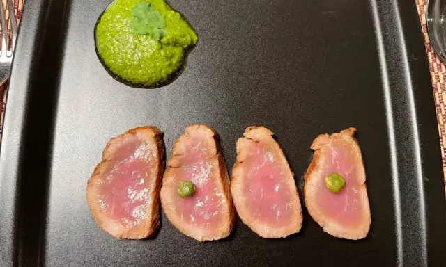 Cuatro lonchas de tataki de salmón con un toque de verde y una guarnición vibrante.