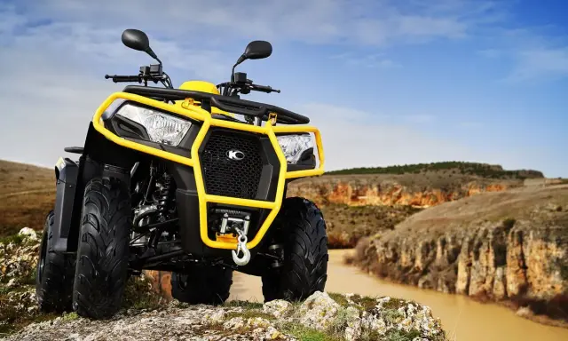 Un quad amarillo listo para conducir por terrenos escarpados junto a un río.