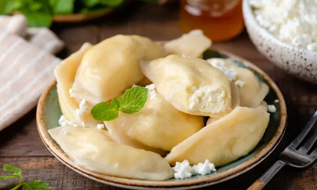 Pyszne pierogi z serem, udekorowane miętą i posypane białym serem. Obok słoiczek miodu i miseczka z serem.