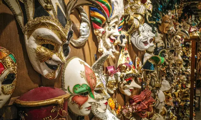 Una parete piena di maschere di carnevale romane, riccamente decorate, pronte per un ballo in maschera.
