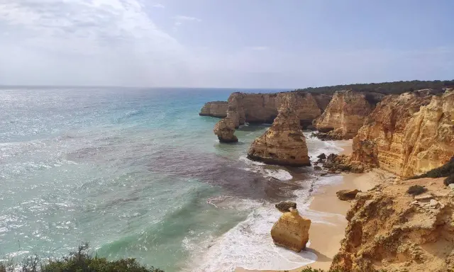 Acantilados dorados y mar turquesa en la ruta de los siete valles colgantes. Olas rompen en la arena de una playa escondida.