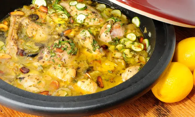 Tajín de pollo con calabacín, aceitunas y almendras, servido en una cazuela de barro, con limones frescos al lado.
